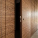 Flush walnut door slightly open in a panelled wall